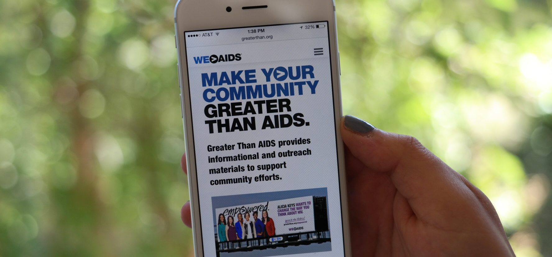 Hand holding a smartphone displaying a graphic reading "Make your community Greater Than HIV"